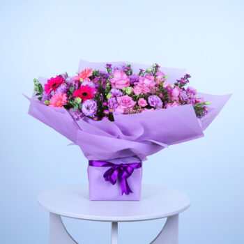 A vibrant purple bouquet tied with a purple ribbon, elegantly displayed on a white table.