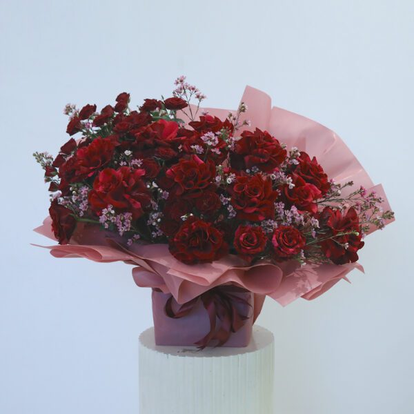 Red rose bouquet wrapped in pink displayed on a table.