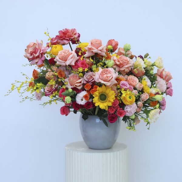 A stunning floral arrangement with roses, sunflowers, and mixed blooms in a modern vase