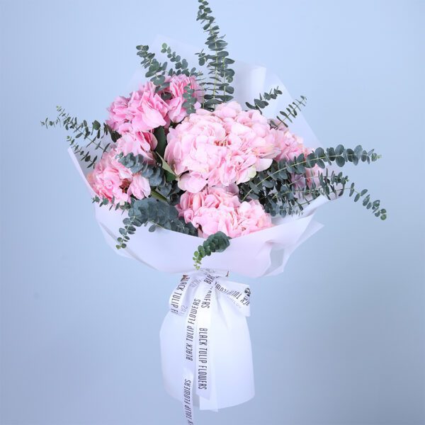 Hand held bouquet of pink carnations with eucalyptus, wrapped in white paper