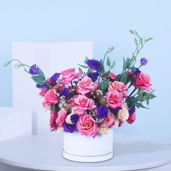 Pink and purple flowers arranged in a stylish white floral box.