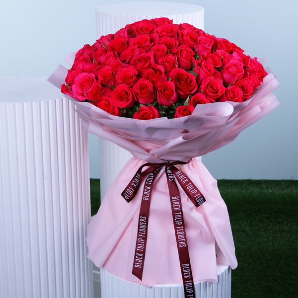 A luxurious bouquet of pink roses wrapped in pink paper and ties with a maroon ribbon.