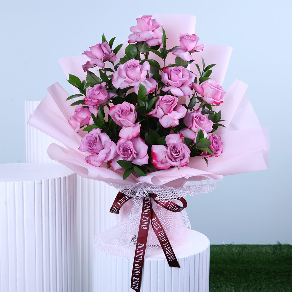 Bouquet of fresh purple roses wrapped in soft pink paper with a ribbon.