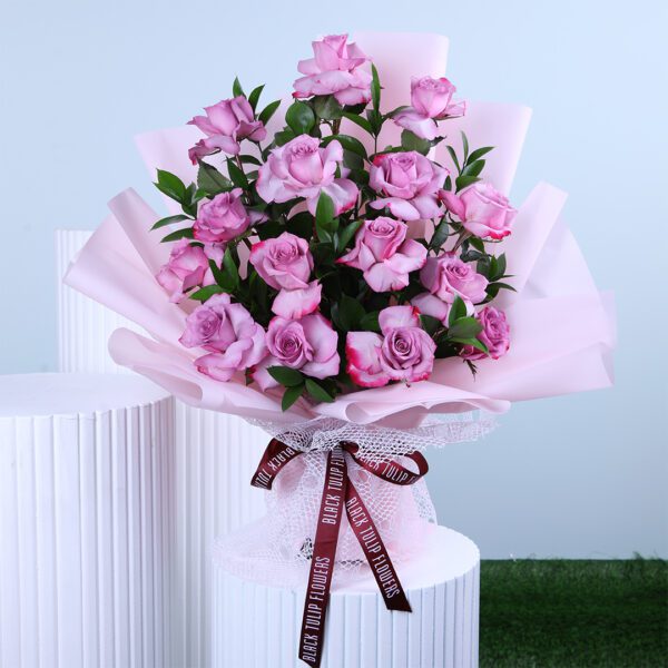 Bouquet of fresh purple roses wrapped in soft pink paper with a ribbon.