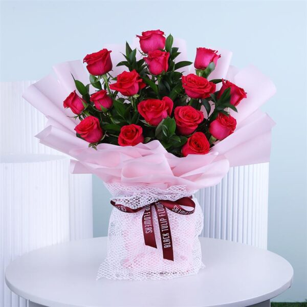 Bouquet of dark pink roses wrapped in soft pink paper with a ribbon placed on a white round table.