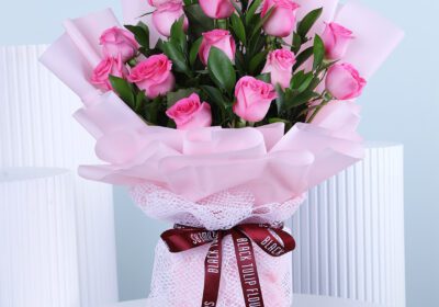 A bouquet of fresh light pink roses wrapped in soft pink paper with a delicate ribbon.