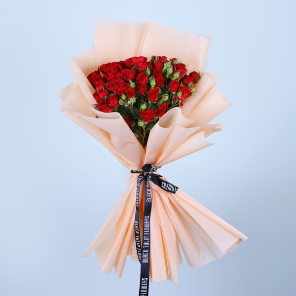 Hand bouquet of fresh red roses wrapped in elegant peach paper.