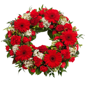 The wreath is composed of red gerbera daisies, red roses, red carnations, and small white flowers with a delicate, branching appearance