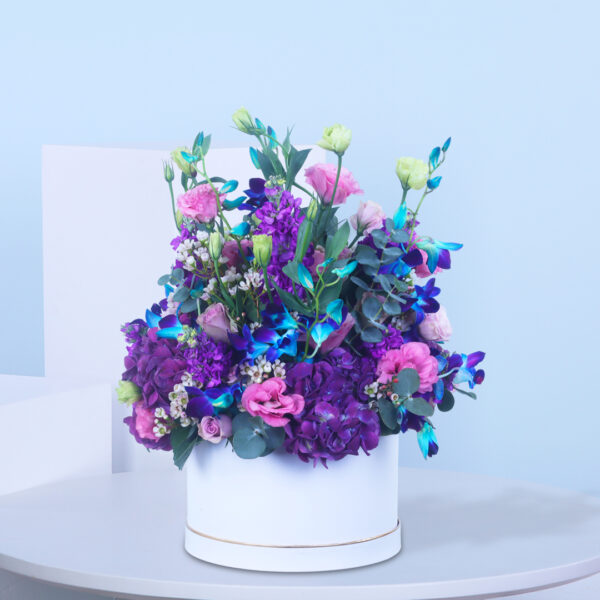 A luxurious floral arrangement featuring purple and pink blooms in a stylish white box