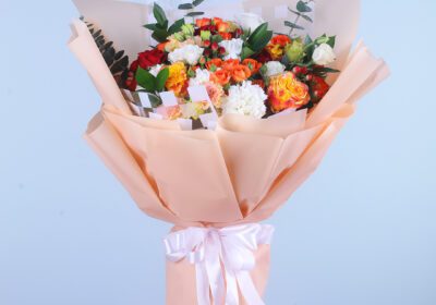 A colorful mixed flower bouquet wrapped in peach and ivory with a satin ribbon.