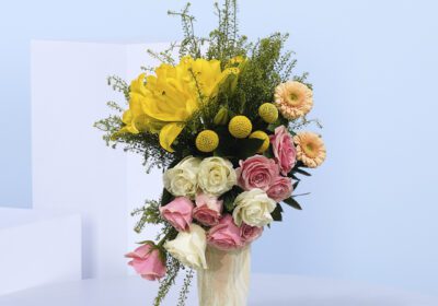 A marble vase filled with yellow lilies, pink and white roses, peach gerberas, and lush greenery.