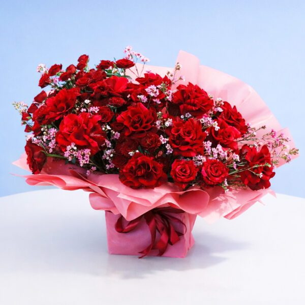 Bouquet featuring red roses and pink flower in blush pink wrapping.