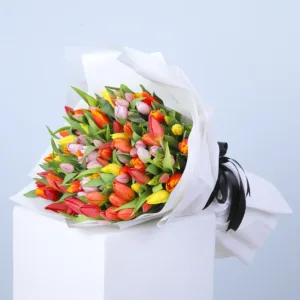 A mixed Tulip bouquet is a vibrant explosion of colors featuring tulips in shades of red, orange, yellow, and pink. The tulips are carefully arranged and wrapped in elegant white paper with a black ribbon, making it a perfect gift for any occasion.