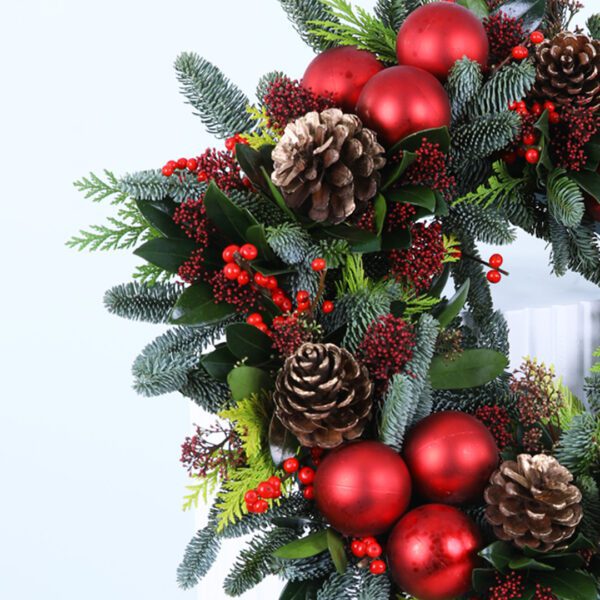 Christmas wreath with evergreens, red ornaments, berries, and pinecones on a white stand.