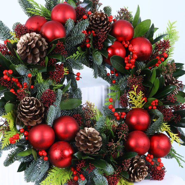 Christmas wreath with evergreens, red ornaments, berries, and pinecones on a white stand.
