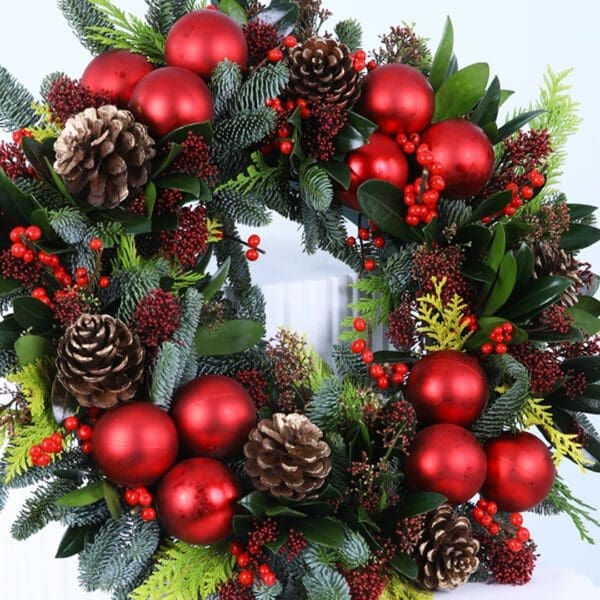 04 Christmas wreath with evergreens, red ornaments, berries, and pinecones on a white stand.