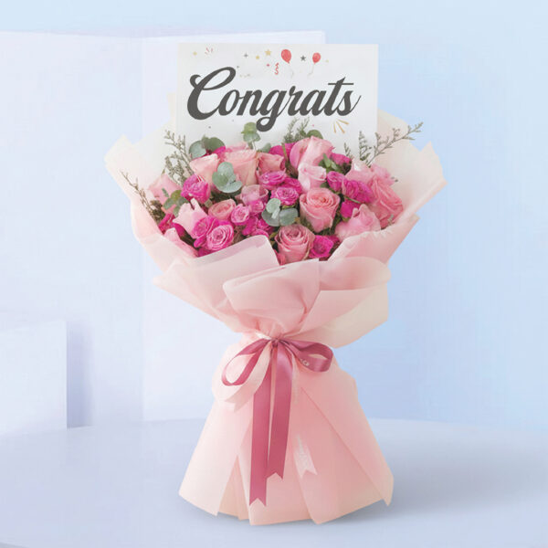 Bouquet featuring hand-tied pink roses, hot pink spray roses & eucalyptus in blush wrap, finished with a “Congrats” card.