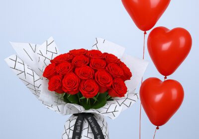 Bouquet of 16 red roses in patterned white wrap, paired with red heart-shaped balloons.