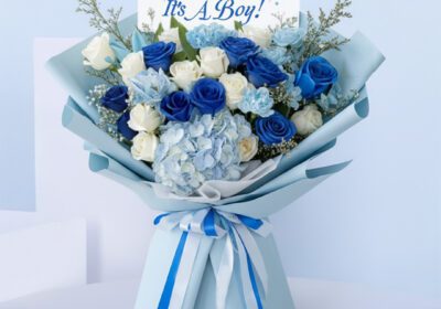 Blue baby boy bouquet with roses, hydrangeas, and other blooms and “It’s a Boy” card.