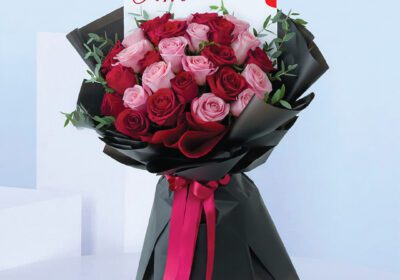 Birthday bouquet with pink and red roses wrapped in black paper and bright ribbon.