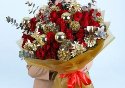 Christmas bouquet with red roses, gold pinecones, golden ornaments, and with festive wrapping