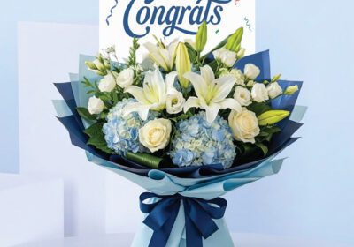 Congrats bouquet with lilies, white roses, blue hydrangeas, and blue wrapping with ribbon.
