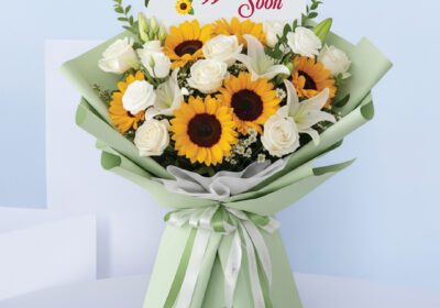 Bouquet featuring hand-tied sunflowers, white roses & lilies in pastel green wrap, finished with a “Get Well Soon” card.