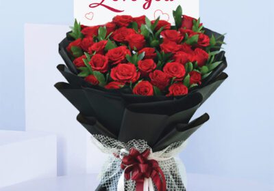 Bouquet featuring hand-tied red roses in elegant black wrap with lace bow, finished with a “Love You” card