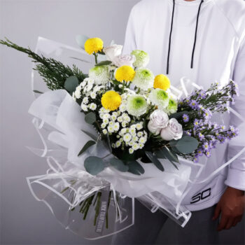 Bouquet featuring hand-tied yellow ping pongs, green ping pongs & purple roses in clear wrap, finished with greenery.