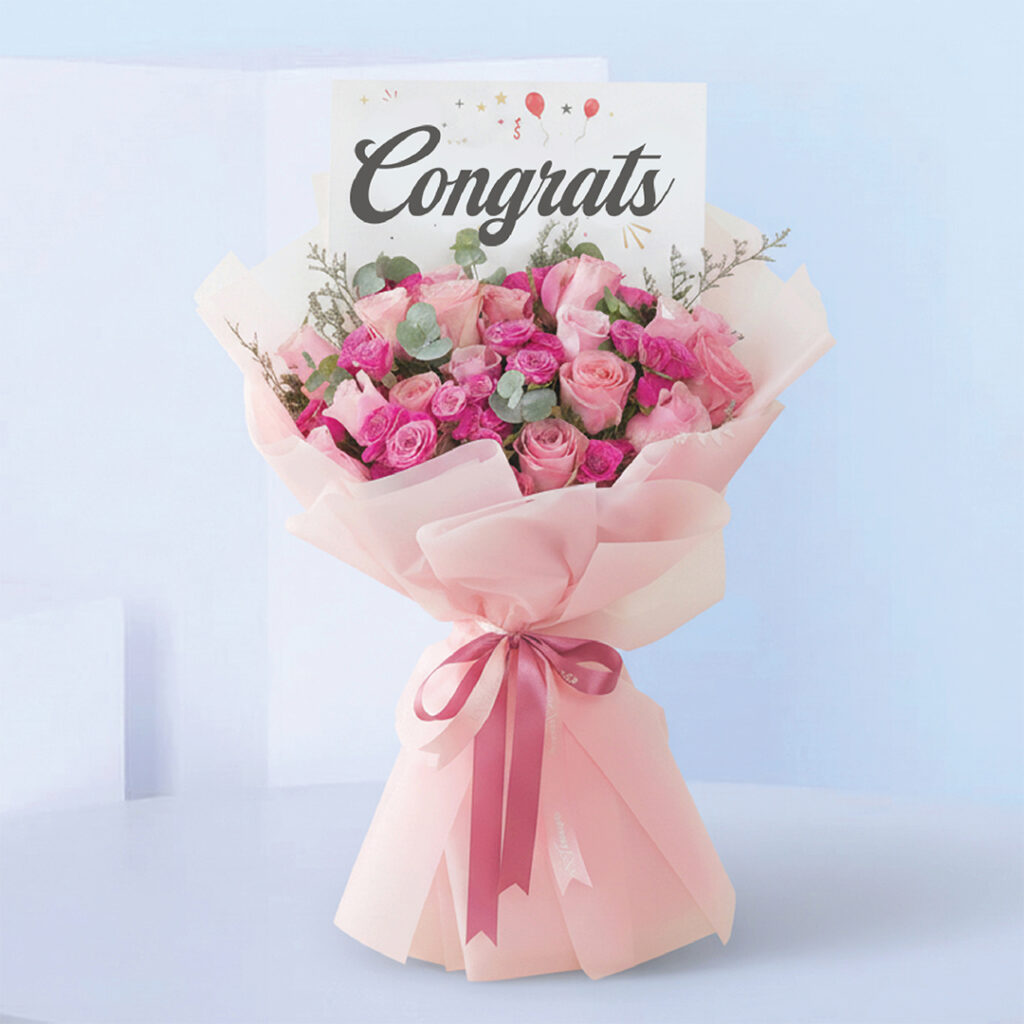 Bouquet featuring hand-tied pink roses, hot pink spray roses & eucalyptus in blush wrap, finished with a “Congrats” card.