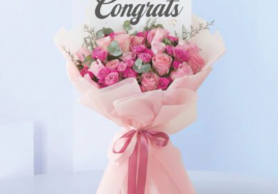 Bouquet featuring hand-tied pink roses, hot pink spray roses & eucalyptus in blush wrap, finished with a “Congrats” card.
