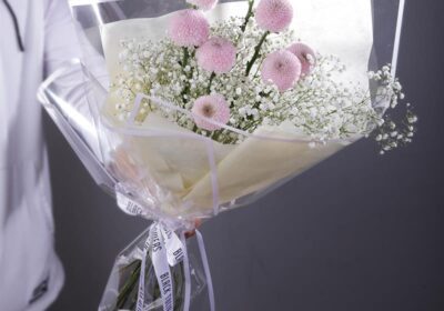 Bouquet featuring hand-tied purple ping pong and baby’s breath in a clear wrap, finished with branded ribbon.