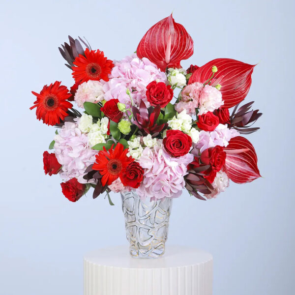 Pink hydrangeas, red anthuriums, red roses, red gerberas and white filler blooms in a clear glass vase arrangement