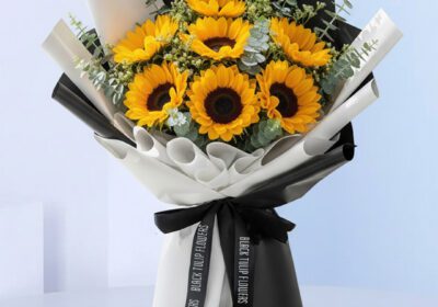 Bouquet featuring hand-tied sunflowers & eucalyptus in black-and-white wrap, finished with a ribbon bow.