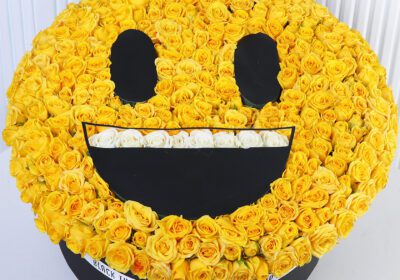 Yellow spray roses arranged in a smiling emoji-style floral box with white rose detailing.