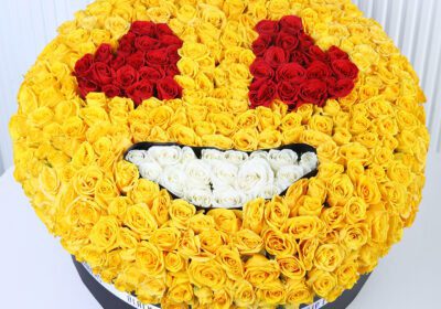Yellow spray roses arranged in a smiley-face floral box design with red and white rose detailing.