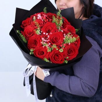 15 red rose bouquet with delicate filler flowers and green foliage in black wrap