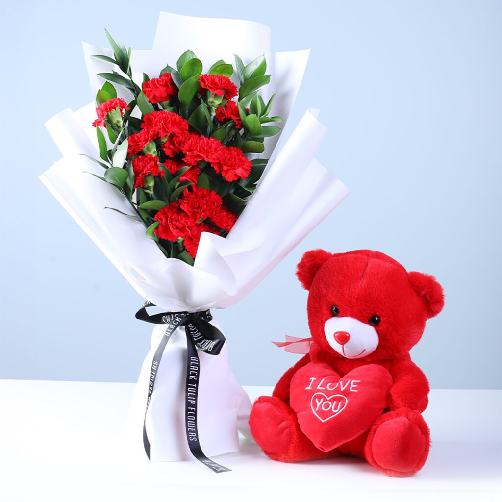 20 red carnations and ruscus greens in premium white wrapping, finished with an “I Love You” teddy.