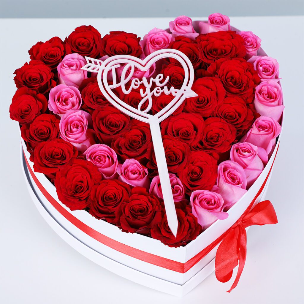 Bouquet of 26 red roses and 18 pink roses in a white heart-shaped gift box with a red ribbon, finished with a “Love You” heart topper.