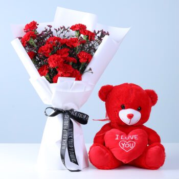 Red carnations with wax flowers in white wrap, paired with a love teddy