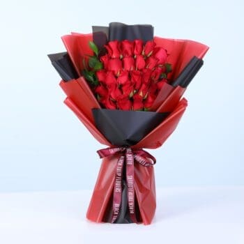 Bouquet of fresh red roses with green foliage in red and black wrapping style, finished with a satin ribbon.
