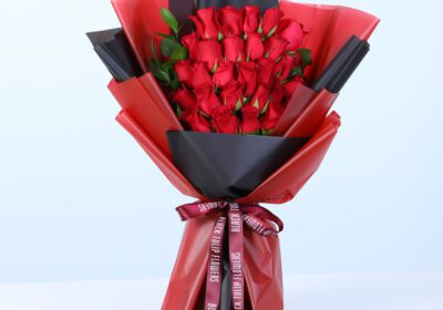 Bouquet of fresh red roses with green foliage in red and black wrapping style, finished with a satin ribbon.