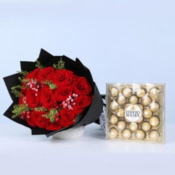 Red roses with filler flowers and green foliage in black wrapping, paired with Ferrero Rocher chocolates.