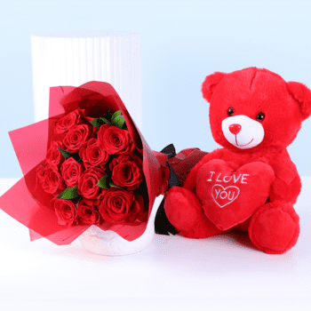 Red teddy bear holding an “I Love You” heart next to a bouquet of red roses wrapped for Valentine’s Day