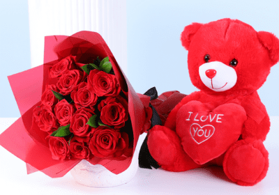 Red teddy bear holding an “I Love You” heart next to a bouquet of red roses wrapped for Valentine’s Day