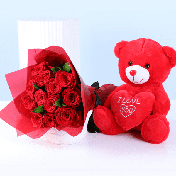 Red teddy bear holding an “I Love You” heart next to a bouquet of red roses wrapped for Valentine’s Day