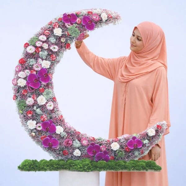 crescent-bloom-harmony Curved crescent floral box with pastel lisianthus, peach carnations, gypsophilia, green trick stems, and purple orchid in a plywood base.