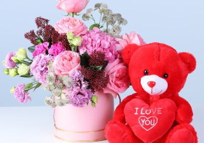 Elegant Pastel Blooms with Teddy featuring pink roses, hydrangea, lisianthus, carnations, and a teddy arranged in a pink hatbox for gifting