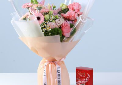 Graceful Pink Celebration Bouquet with Lindt featuring pink gerberas, roses, lilies, hydrangea, and seasonal flowers arranged with chocolate for gifting