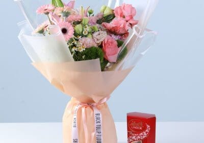 Graceful Pink Celebration Bouquet with Lindt featuring pink gerberas, roses, lilies, hydrangea, and seasonal flowers arranged with chocolate for gifting